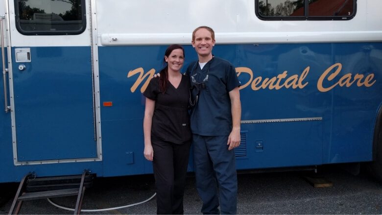Doctor Altenbach with a dental team member next to a blue and white bus
