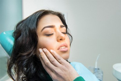 Patient in Beauclerc holding cheek at dentist