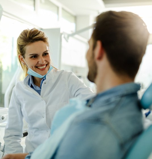 Smiling dentist talking to patient in treatment chair